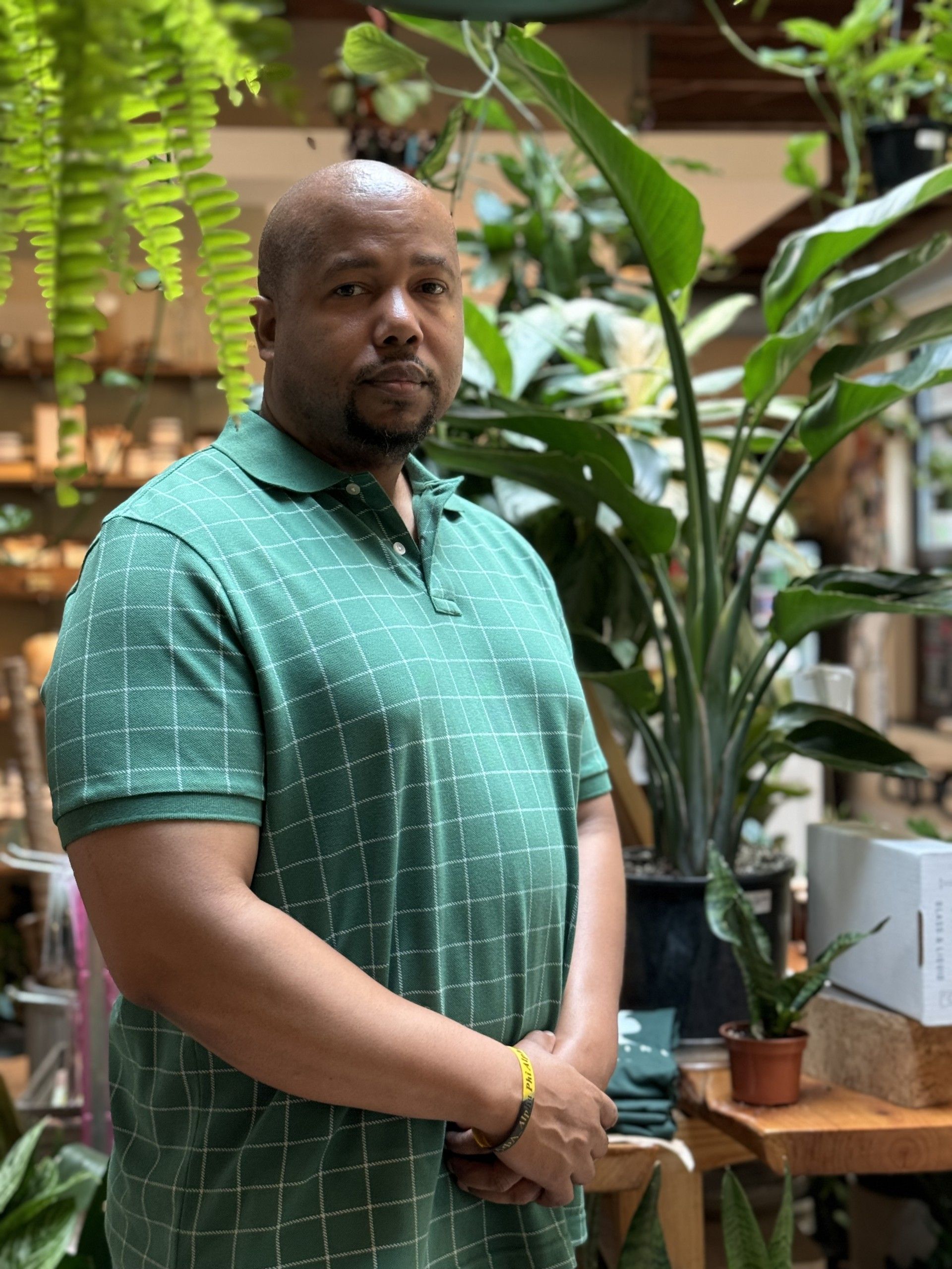 A woman in a green shirt and black skirt is standing in front of a bunch of plants. - WrightNow Counseling – Philadelphia, PA