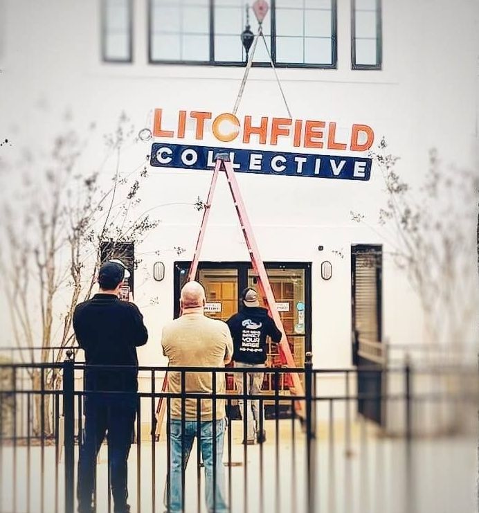 Litchfield Collective sign being installed above building entrance; three men watch.