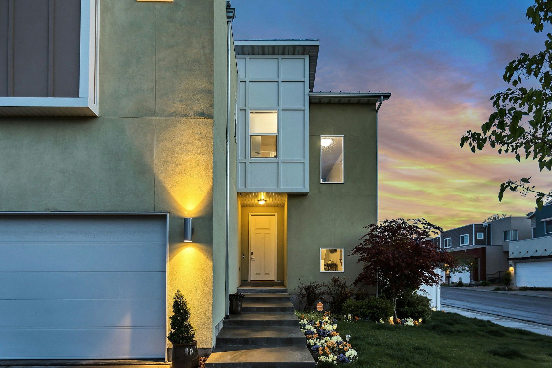 Modern two-story house exterior with front door, garage, and evening sky. Soft lighting illuminates the entryway.