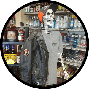 Skeleton wearing a hat, leather jacket, and t-shirt, posing in a liquor store.
