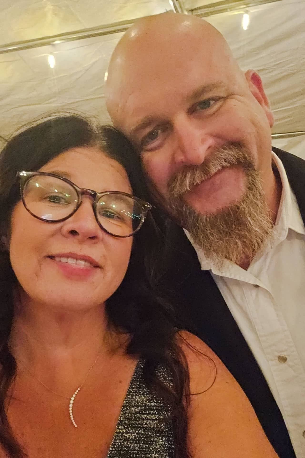 A man and a woman are posing for a picture and the woman is wearing glasses.