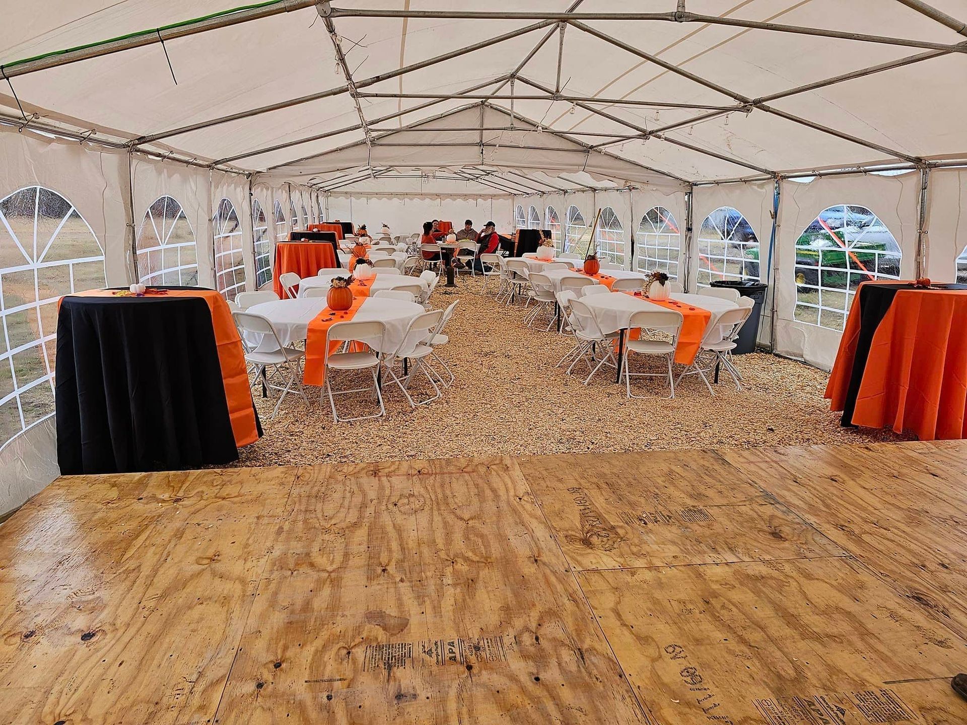 A large tent filled with tables and chairs and a wooden dance floor.