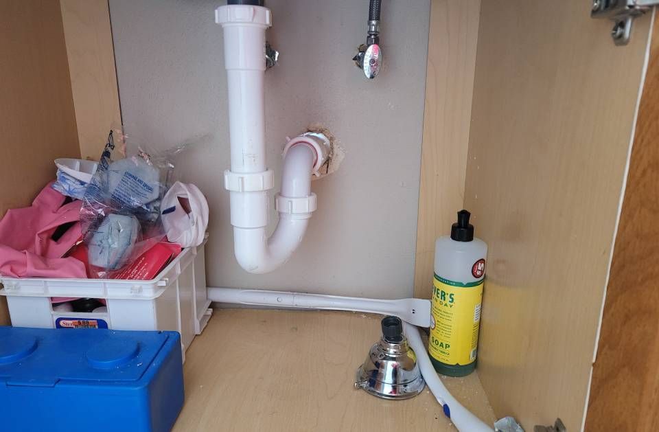 A sink with a bottle of dish soap and a basket of cleaning supplies underneath it.