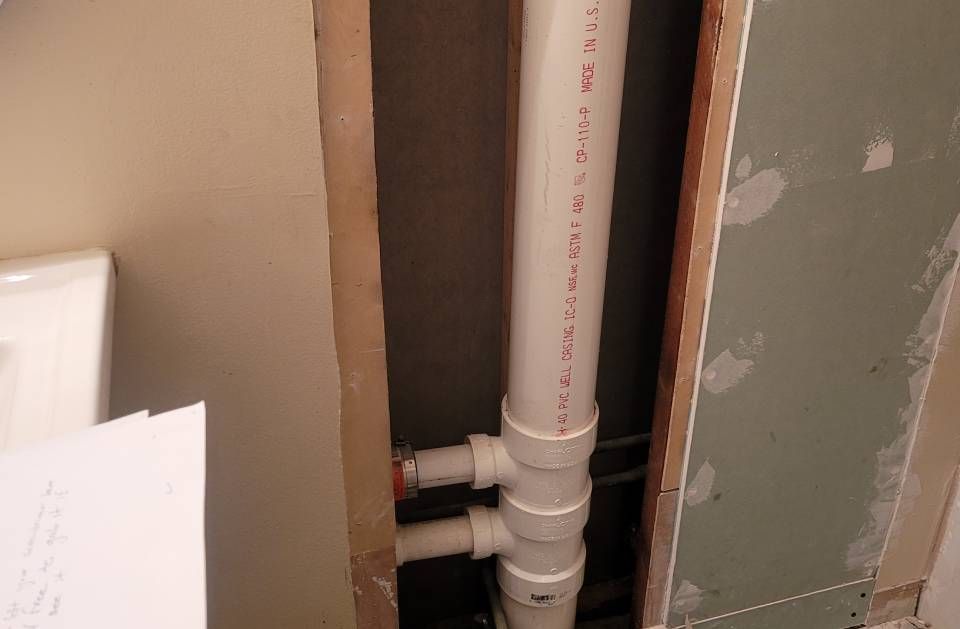 A white pipe with red writing on it is being installed in a wall.