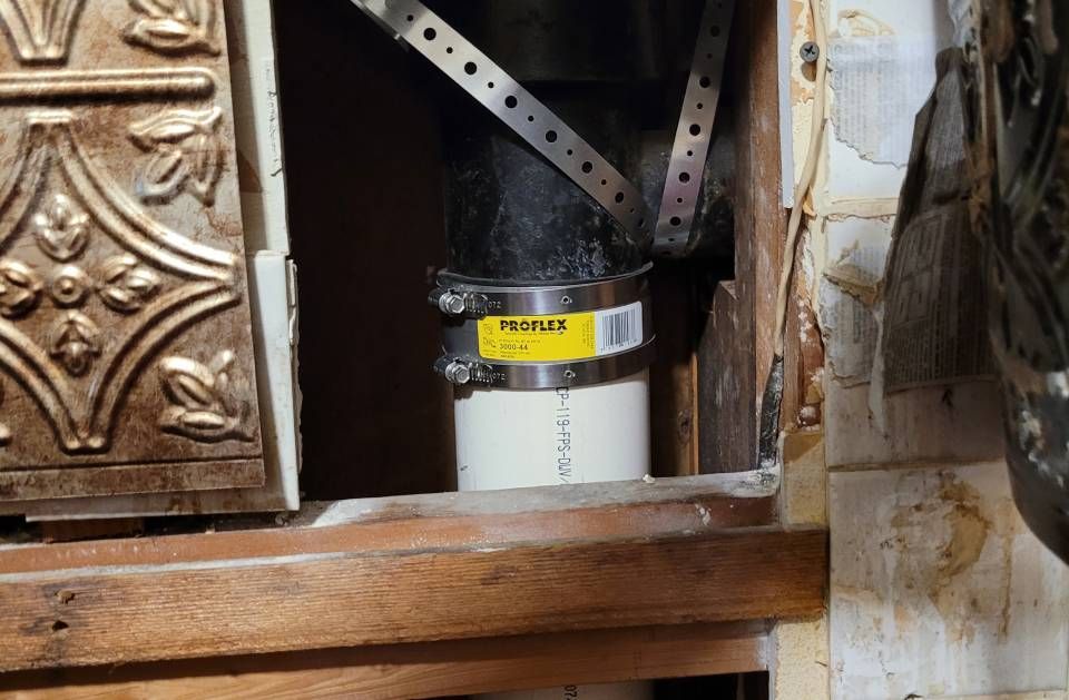 A pipe with a clamp on it is sitting in a hole in a wall.