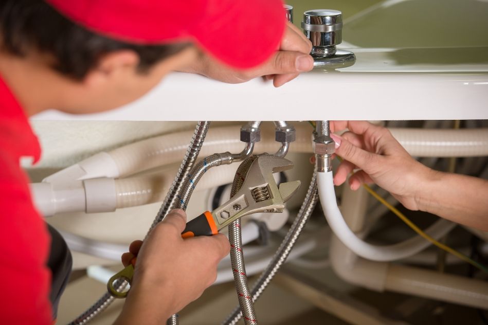 A plumber is fixing a sink with a wrench.