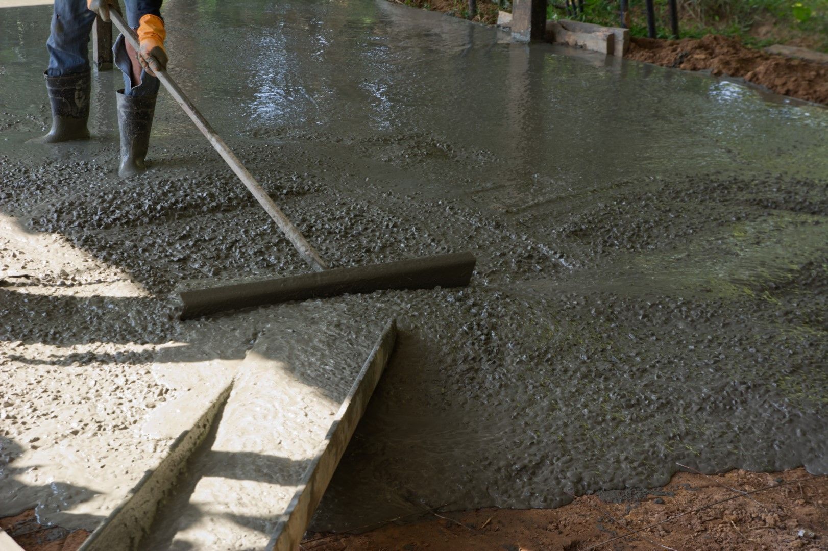 A man is raking a concrete driveway with a broom.