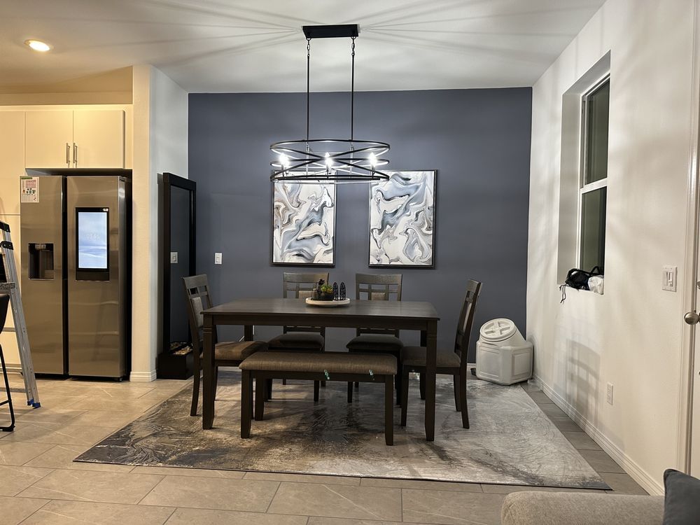 Dining room with table, chairs, art, rug, and modern chandelier against a gray wall.