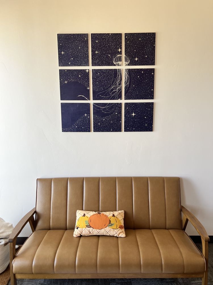 A brown couch below a nine-panel starry night art installation. A pumpkin pillow rests on the couch.