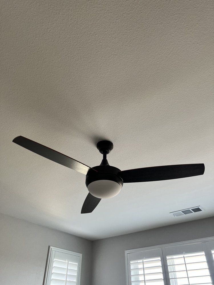 Ceiling fan with three black blades and a central light fixture, mounted on a white ceiling.