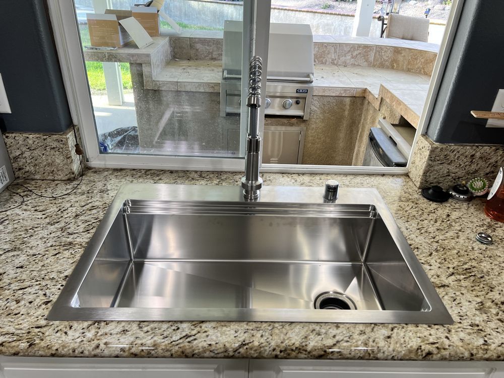 Stainless steel kitchen sink installed in granite countertop, with an outdoor kitchen view.