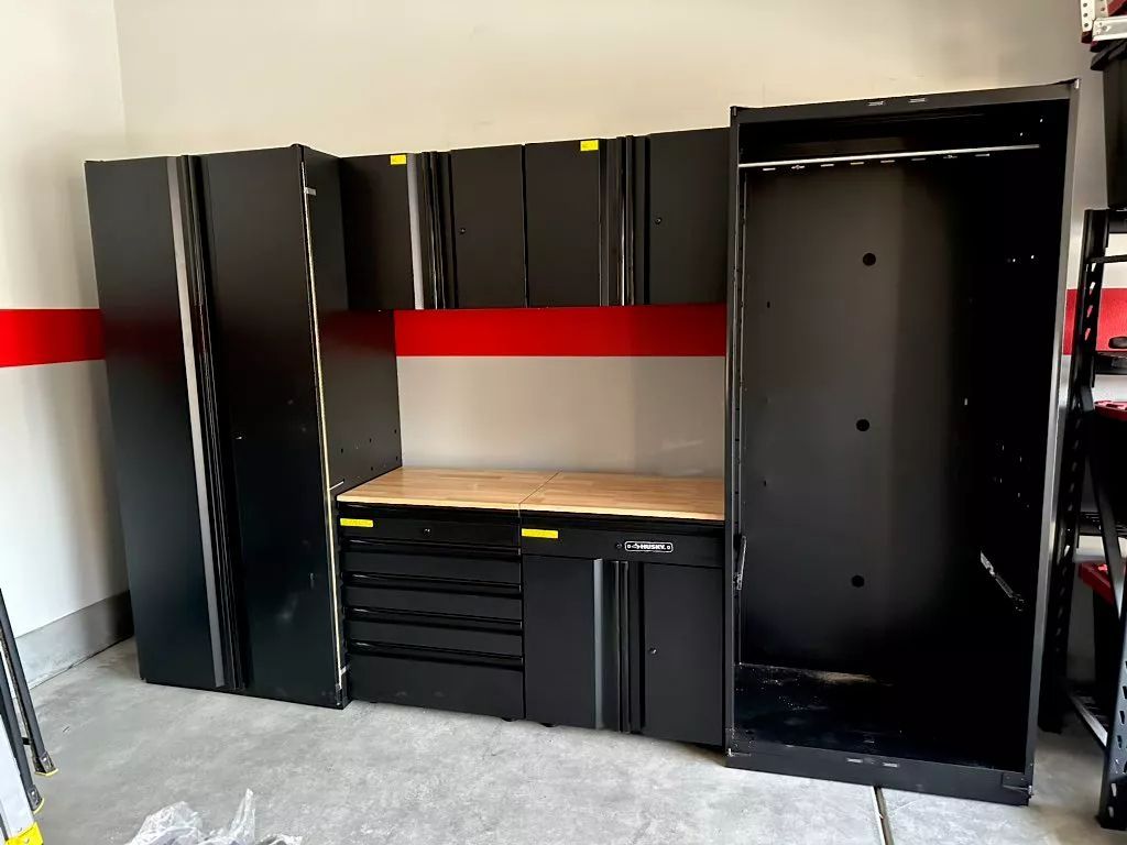 Black garage cabinets, including tall lockers and a workbench, against a red and white wall.