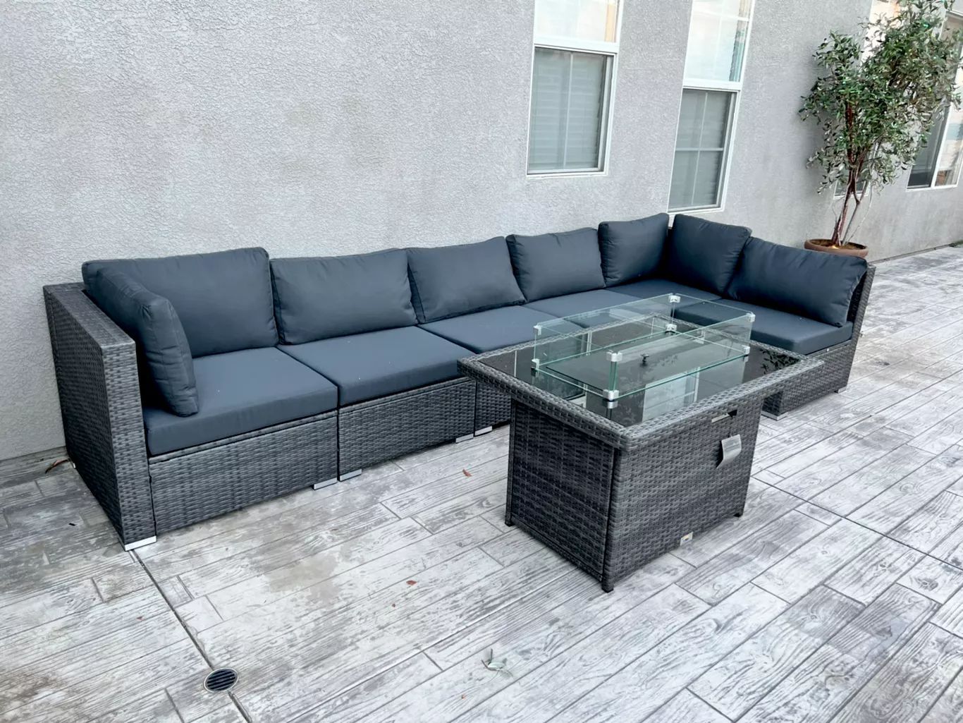 Gray outdoor sectional sofa with fire pit on a concrete patio.