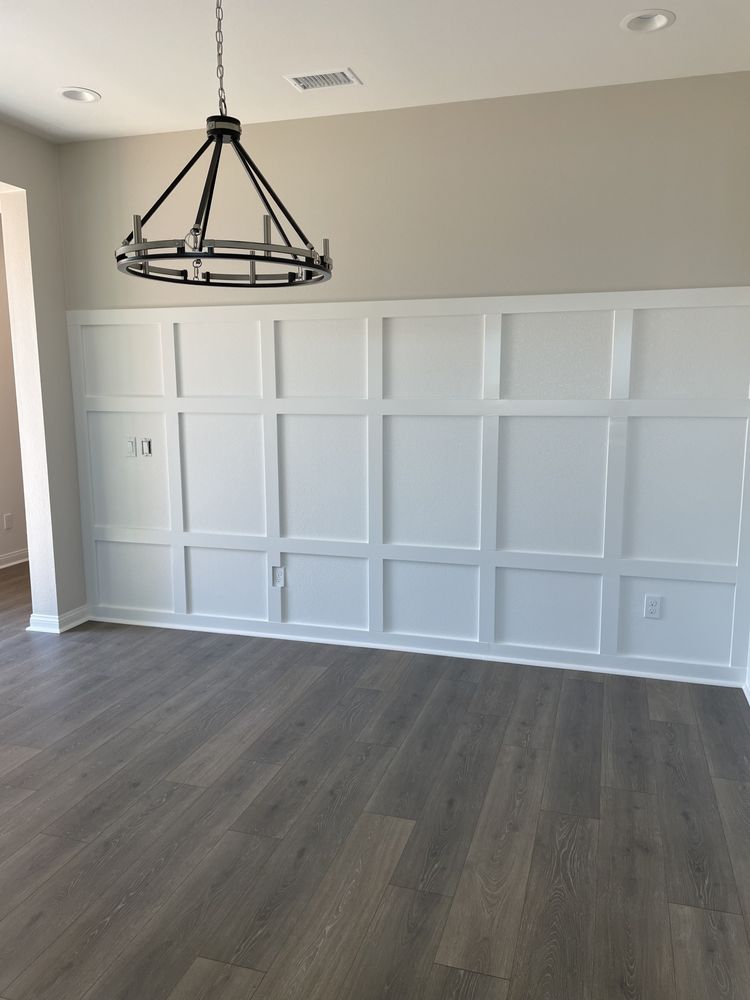 White paneled wall with a decorative chandelier, gray flooring.