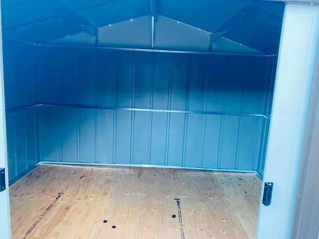 Inside of a metal shed with a wooden floor, blue walls, and an open doorway.