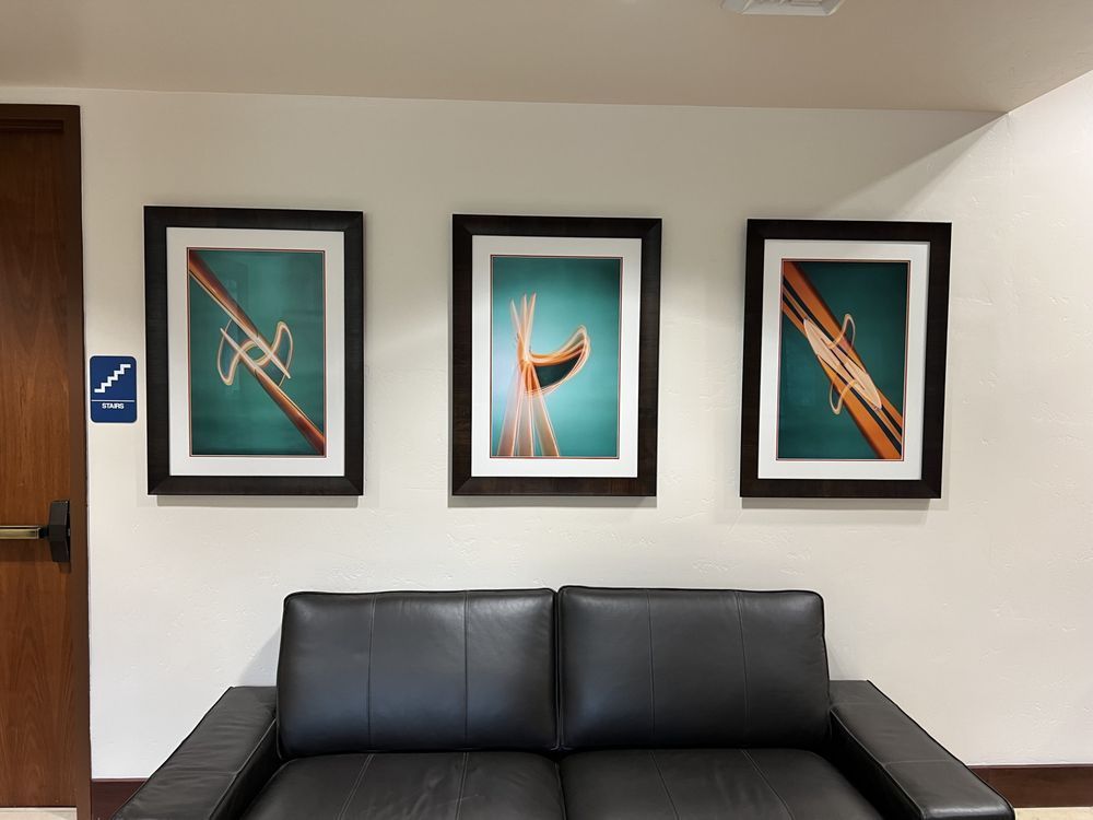 Three framed abstract art pieces above a black leather sofa against a white wall; restroom sign on the left.