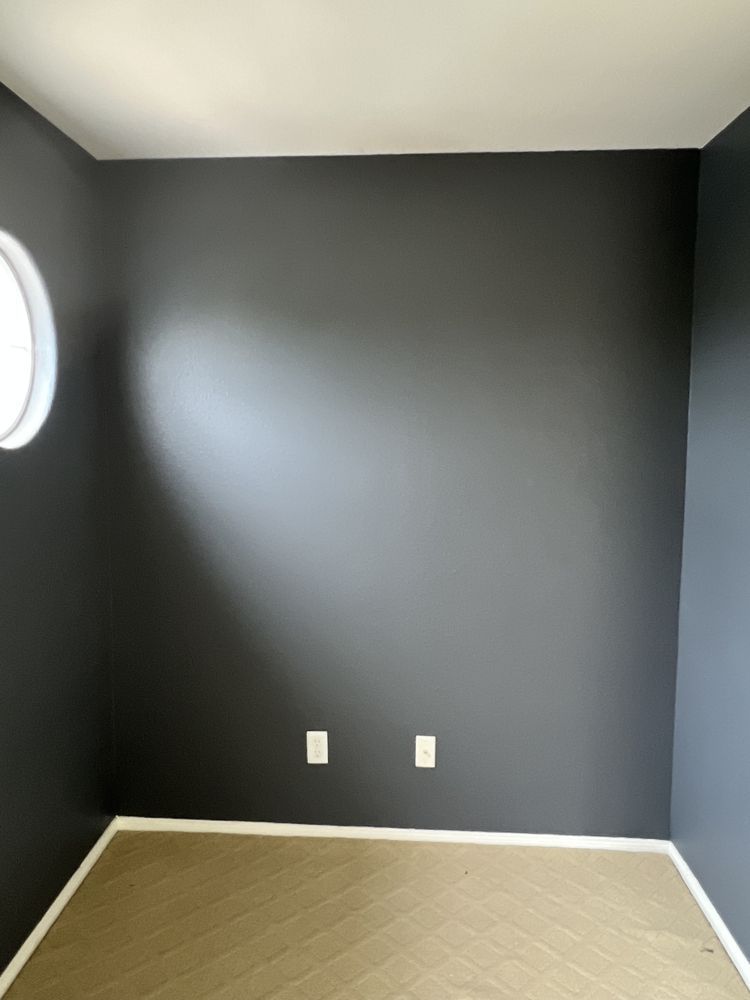 Dark gray room with a round window, two electrical outlets, and beige carpet.