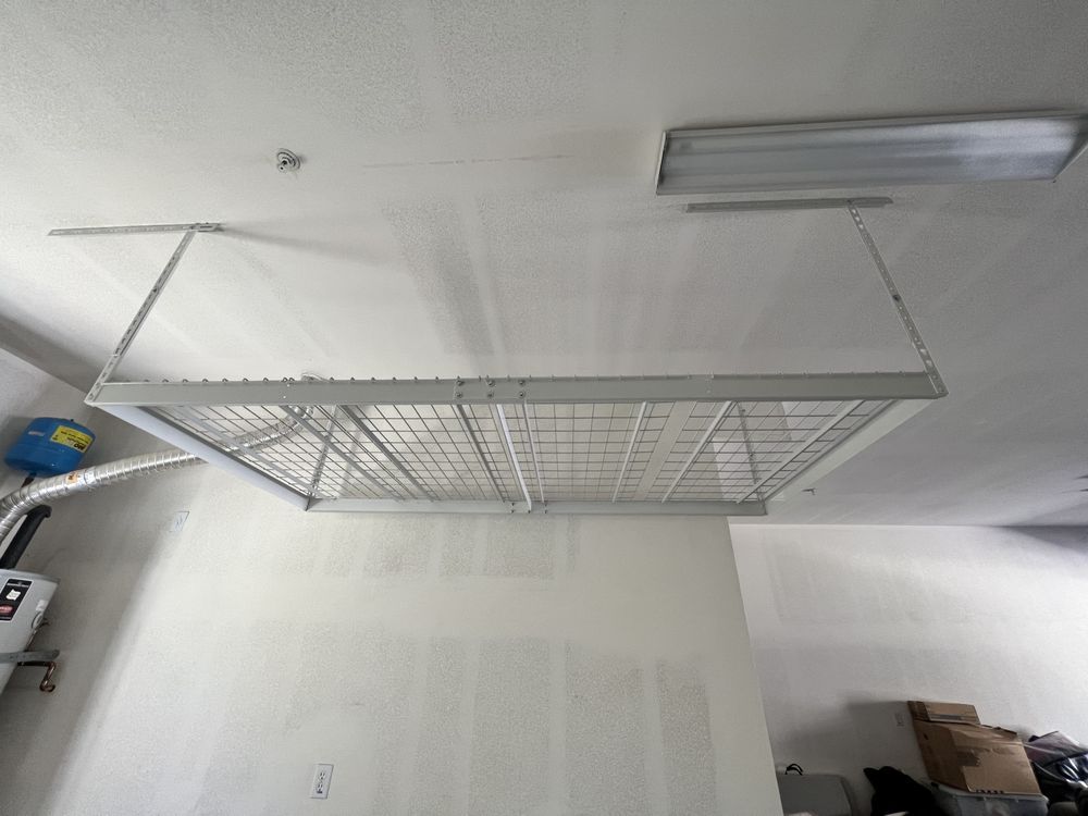 White wire-mesh overhead storage shelf mounted to the ceiling in a garage.
