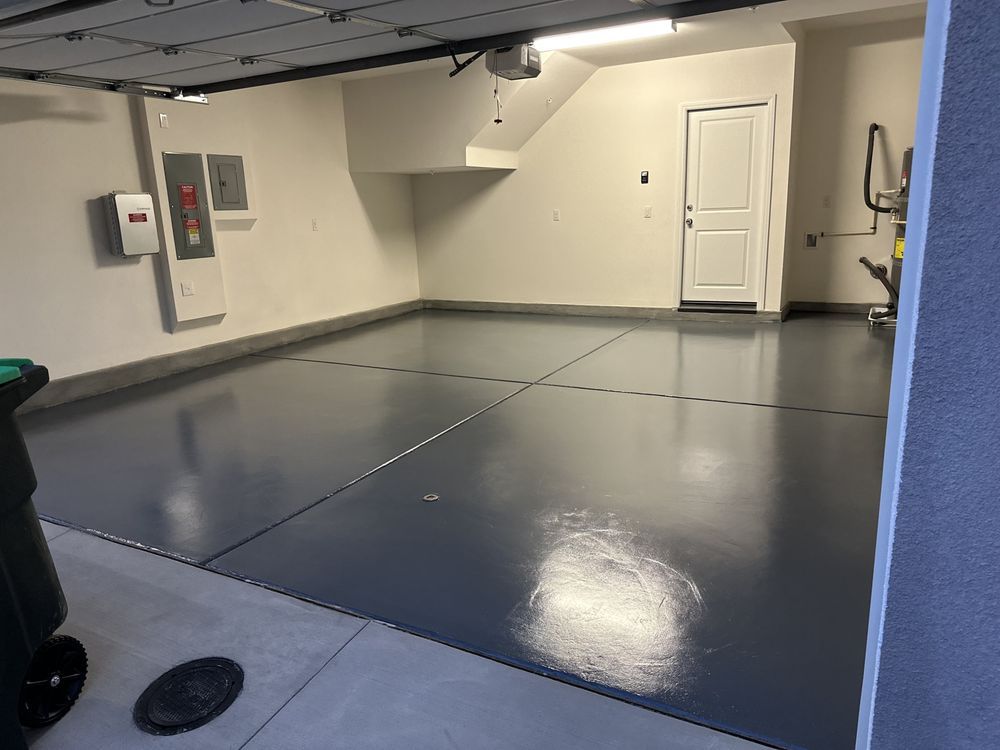Empty garage with a gray, epoxy-coated floor, white walls, and a closed white door.