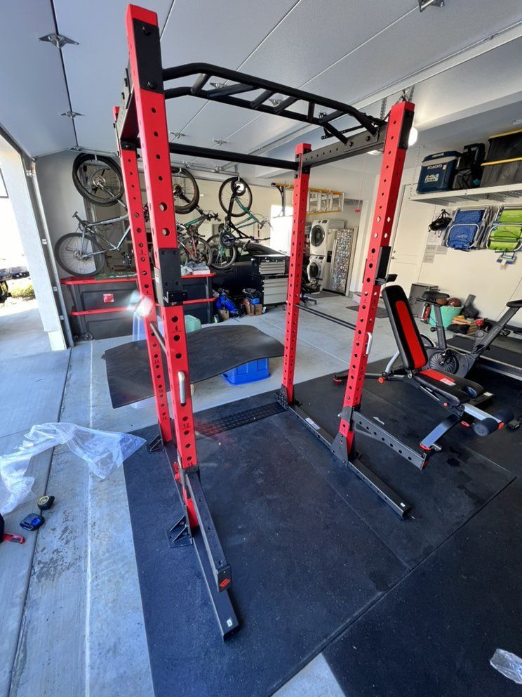Red and black weightlifting power rack in a garage gym with exercise equipment.