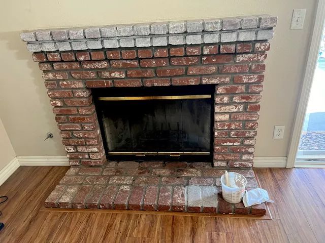 Brick fireplace with a black framed firebox, white painted top, and hardwood floor.