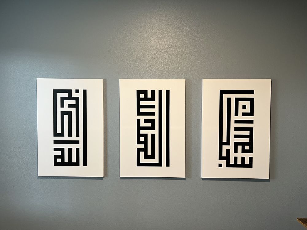Three framed artworks with black Arabic calligraphy on white backgrounds, hung on a gray wall.