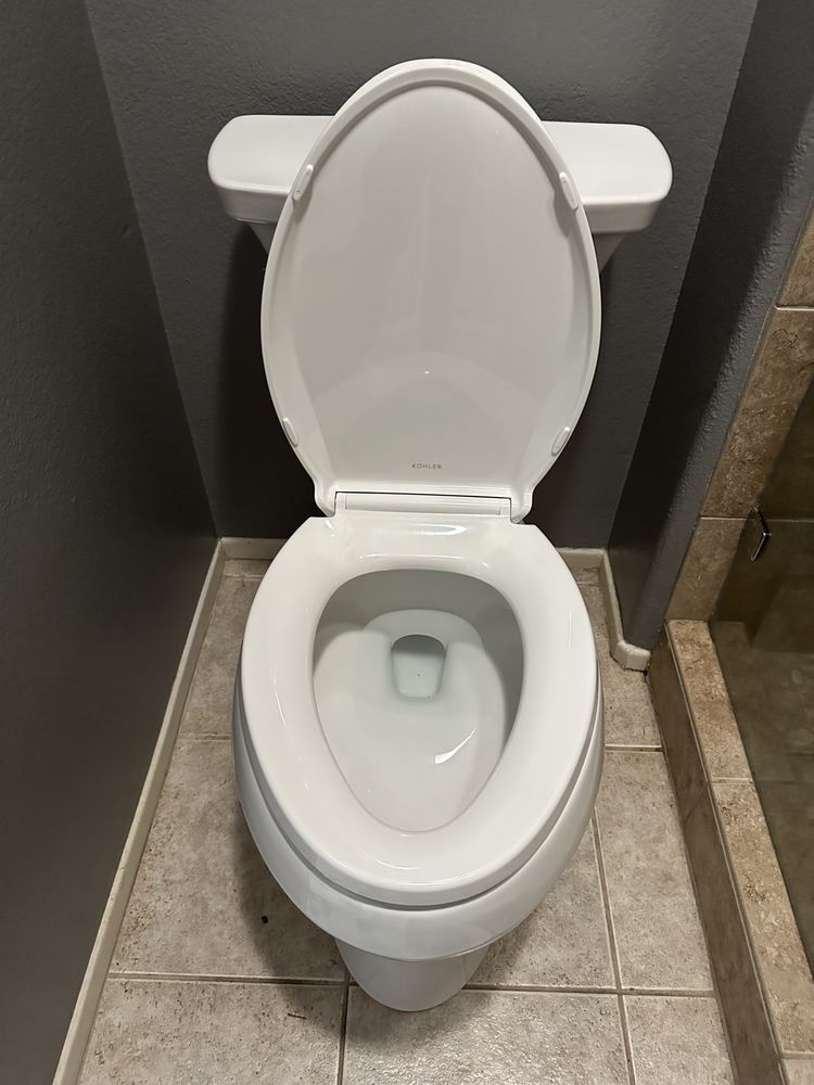 White toilet with seat up against gray wall, sitting on tile floor.