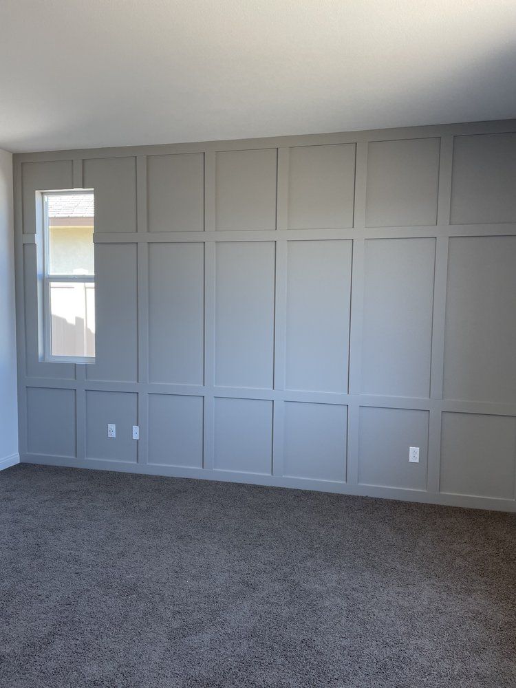 Grey paneled wall with a window, in a room with brown carpet.