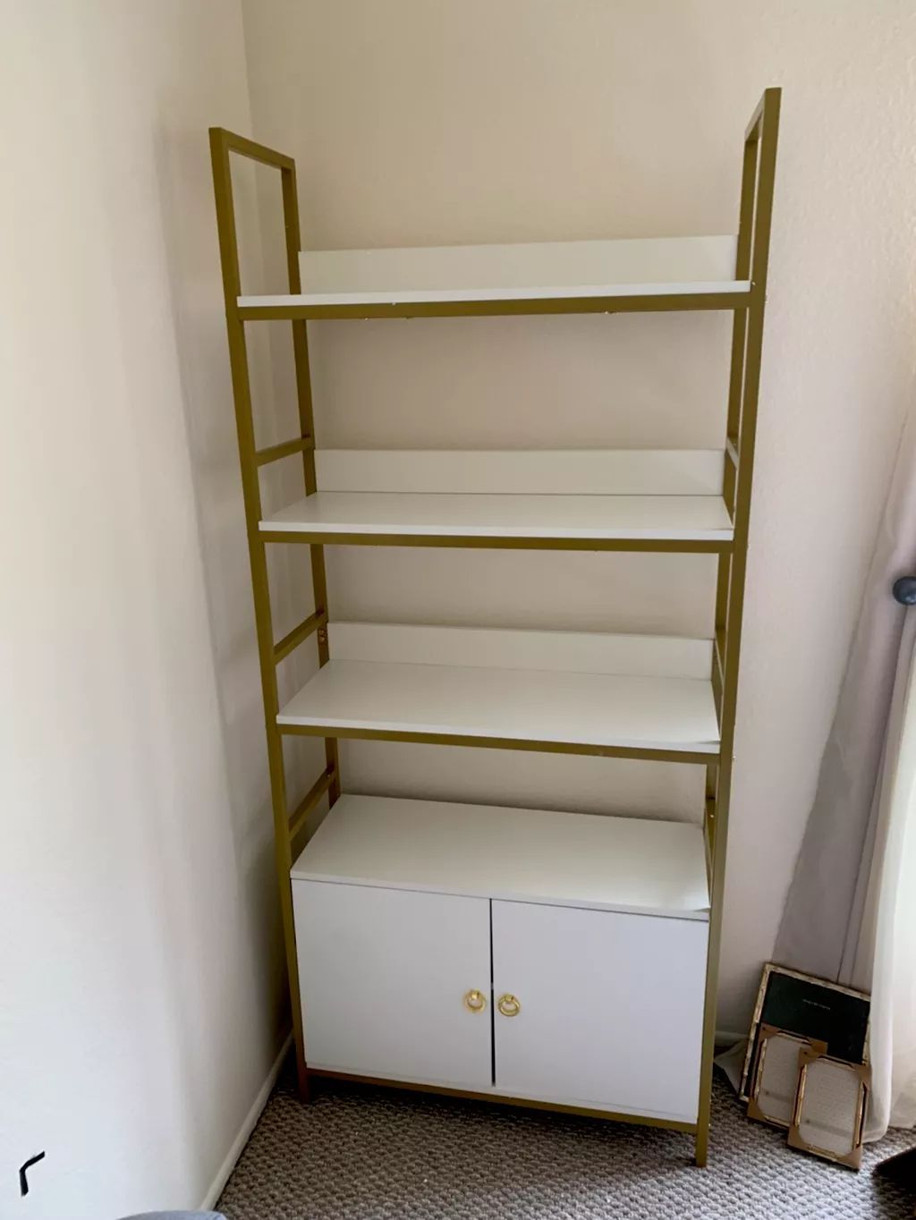Gold and white bookshelf with four shelves and a cabinet.