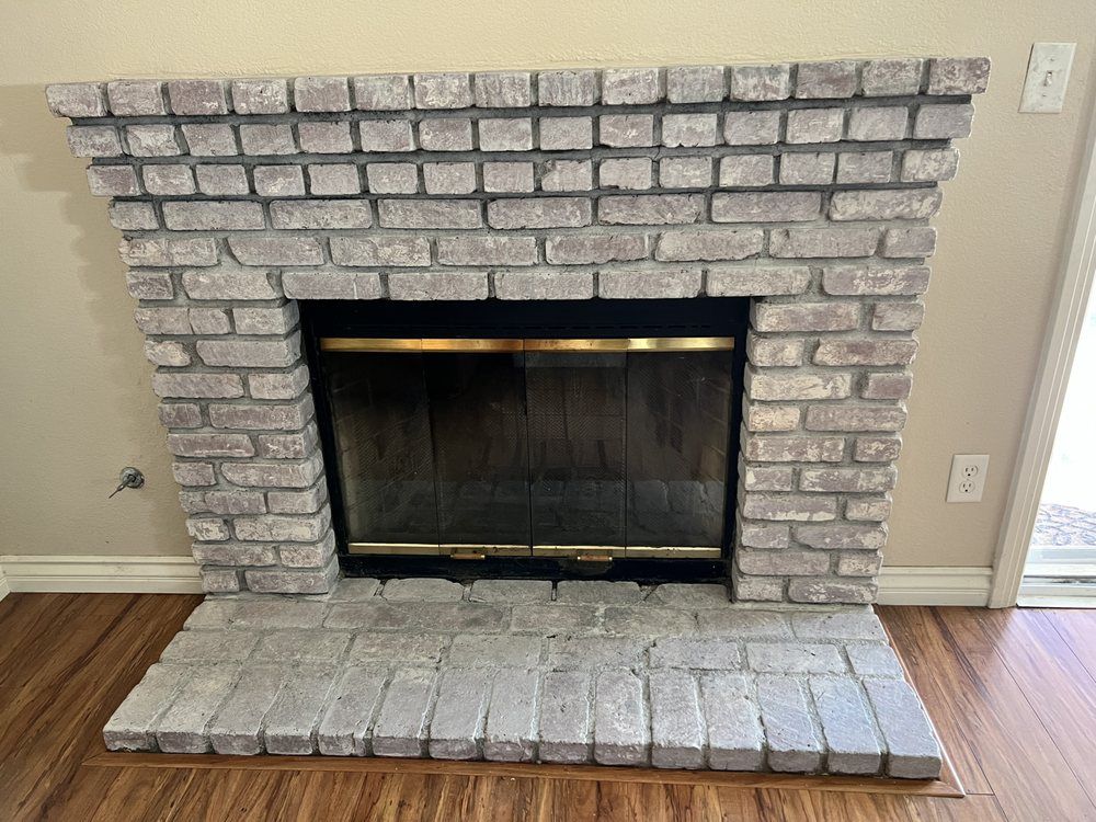 Brick fireplace with painted gray bricks, black glass screen, and wooden floors.