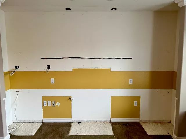 Empty room with mustard yellow and white painted walls, electrical outlets, and a black line.