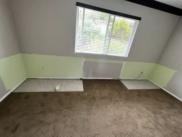 An interior room with angled walls, a window, and brown carpet. Green paint on lower walls.