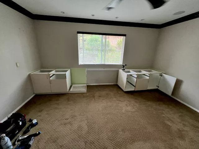 Room with brown carpet, white cabinets, and a window with blinds.