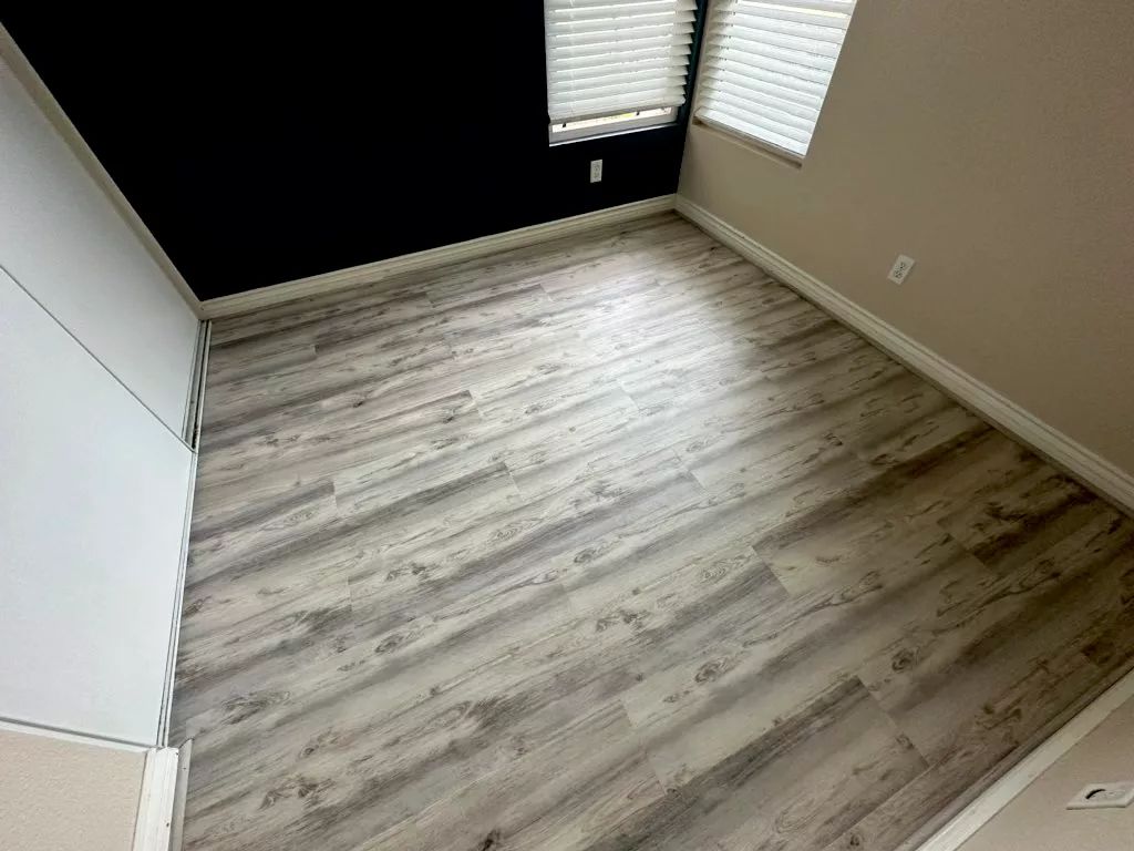 Empty room with gray wood-look flooring, black wall, white trim, and a window with blinds.