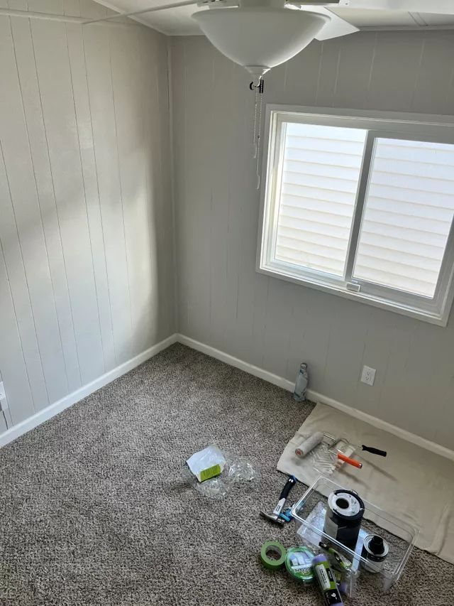 A room with gray walls and carpet, a window, and painting supplies.