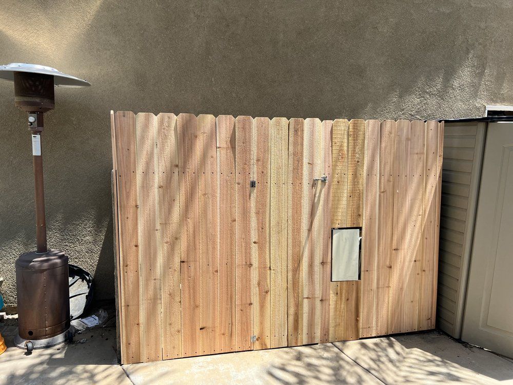 Wooden fence section with small rectangular cutout, standing outdoors next to a propane heater.