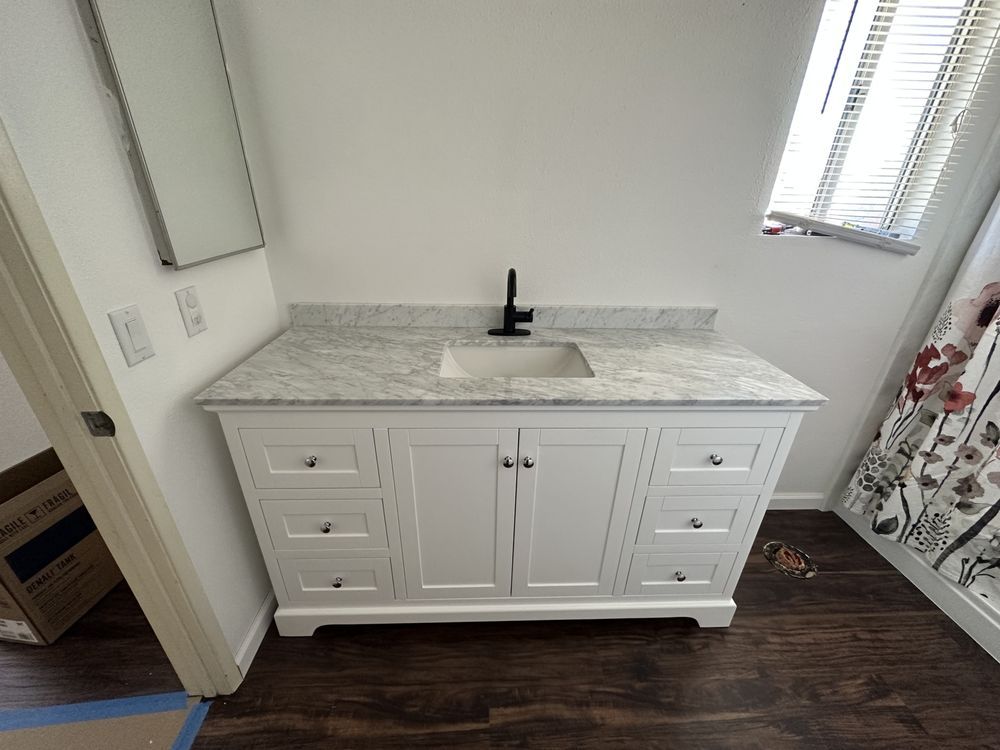White bathroom vanity with marble countertop, black faucet, and white cabinets against a white wall.