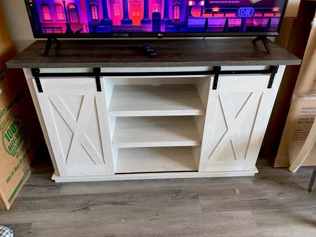 White and brown TV stand with sliding barn doors and shelves, with a TV on top.