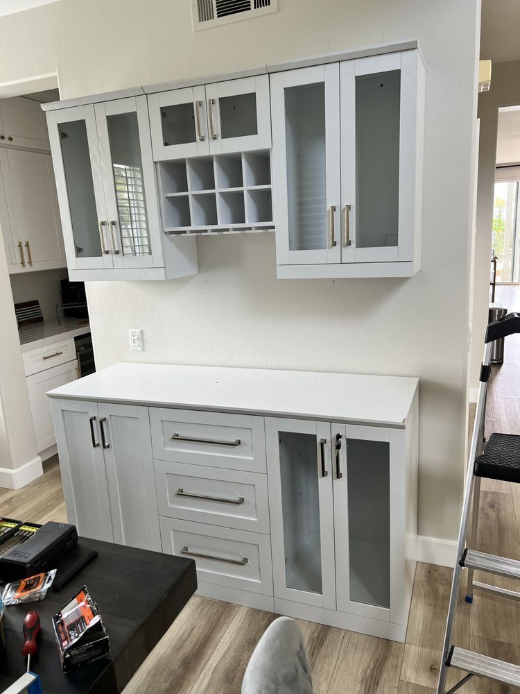 Built-in white cabinets with countertop, wine rack, and glass-front doors against a white wall.