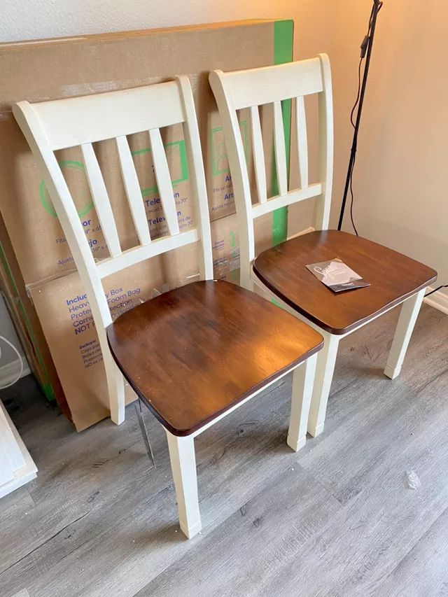 Two wooden chairs with cream-colored frames and brown seats, against a cardboard box.