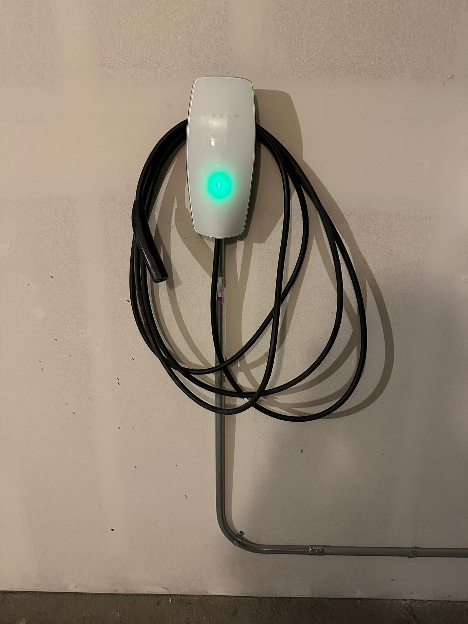 White EV charger mounted on a wall; green light indicates readiness; coiled black cable.