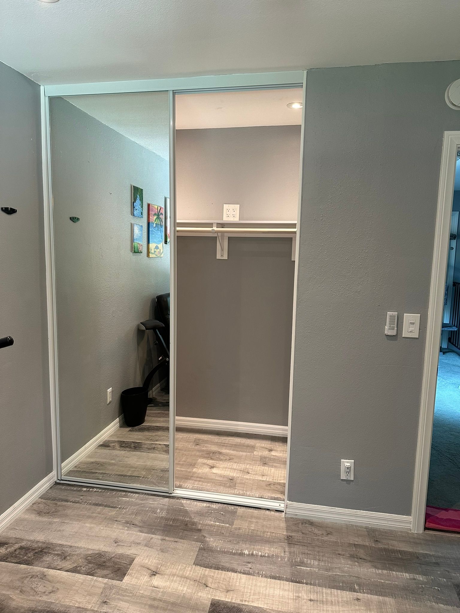 Mirrored closet doors in a gray room. Light wooden floor. Closet interior is visible.
