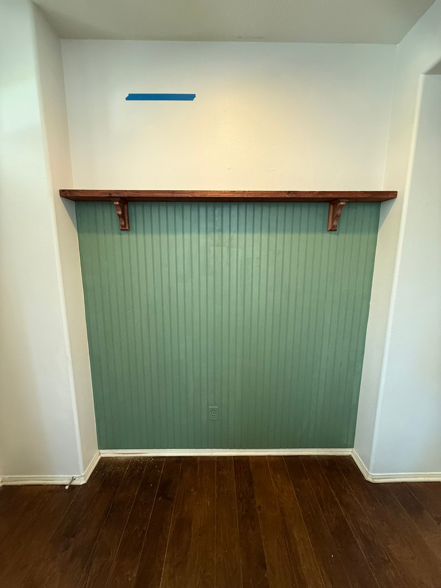 Green paneled accent wall with a wooden shelf and dark wood floor.
