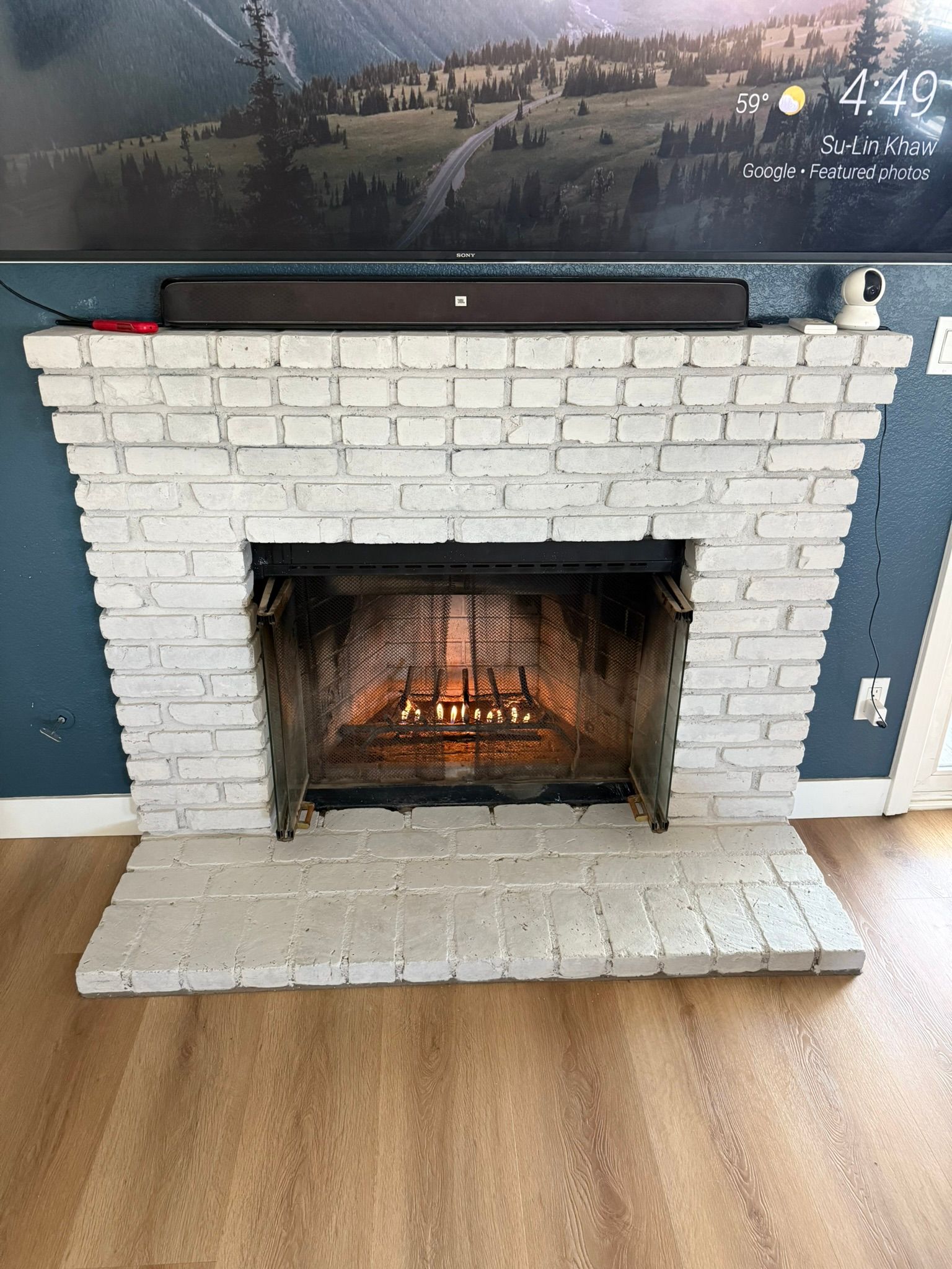 White painted brick fireplace with a soundbar above the firebox, with fire burning inside.