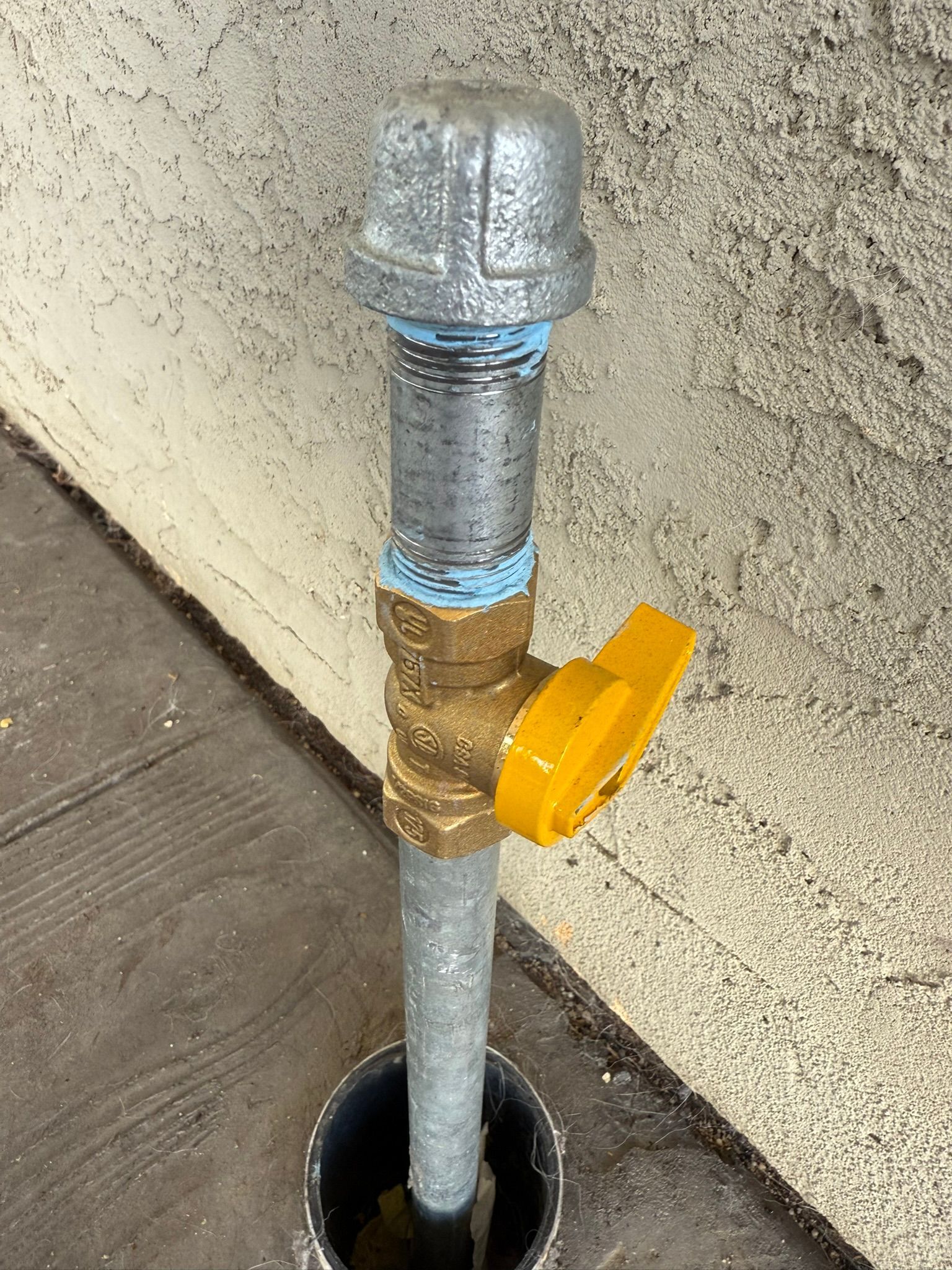A gas shut-off valve with a yellow handle, above ground level, next to a building.