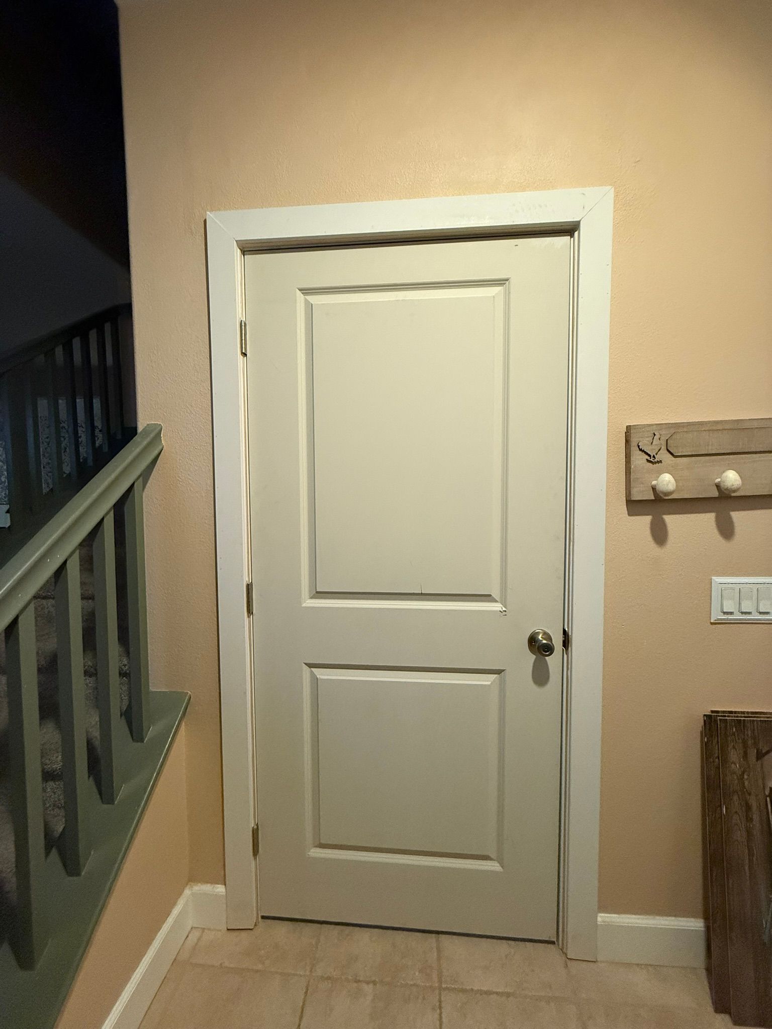 White door set in a beige wall, next to a stairway and coat rack.