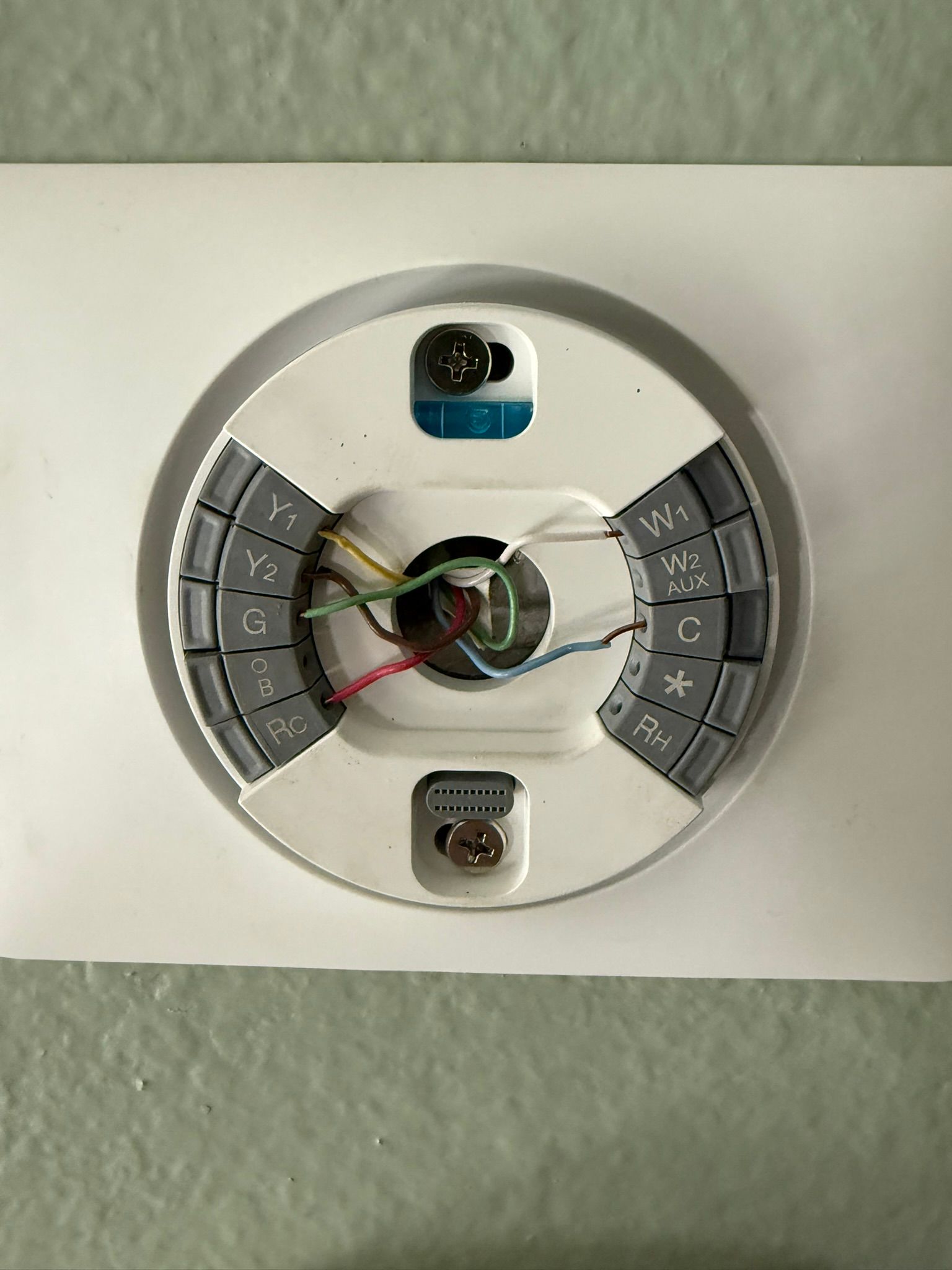 White Nest thermostat base, wires connected to terminals on a white wall.