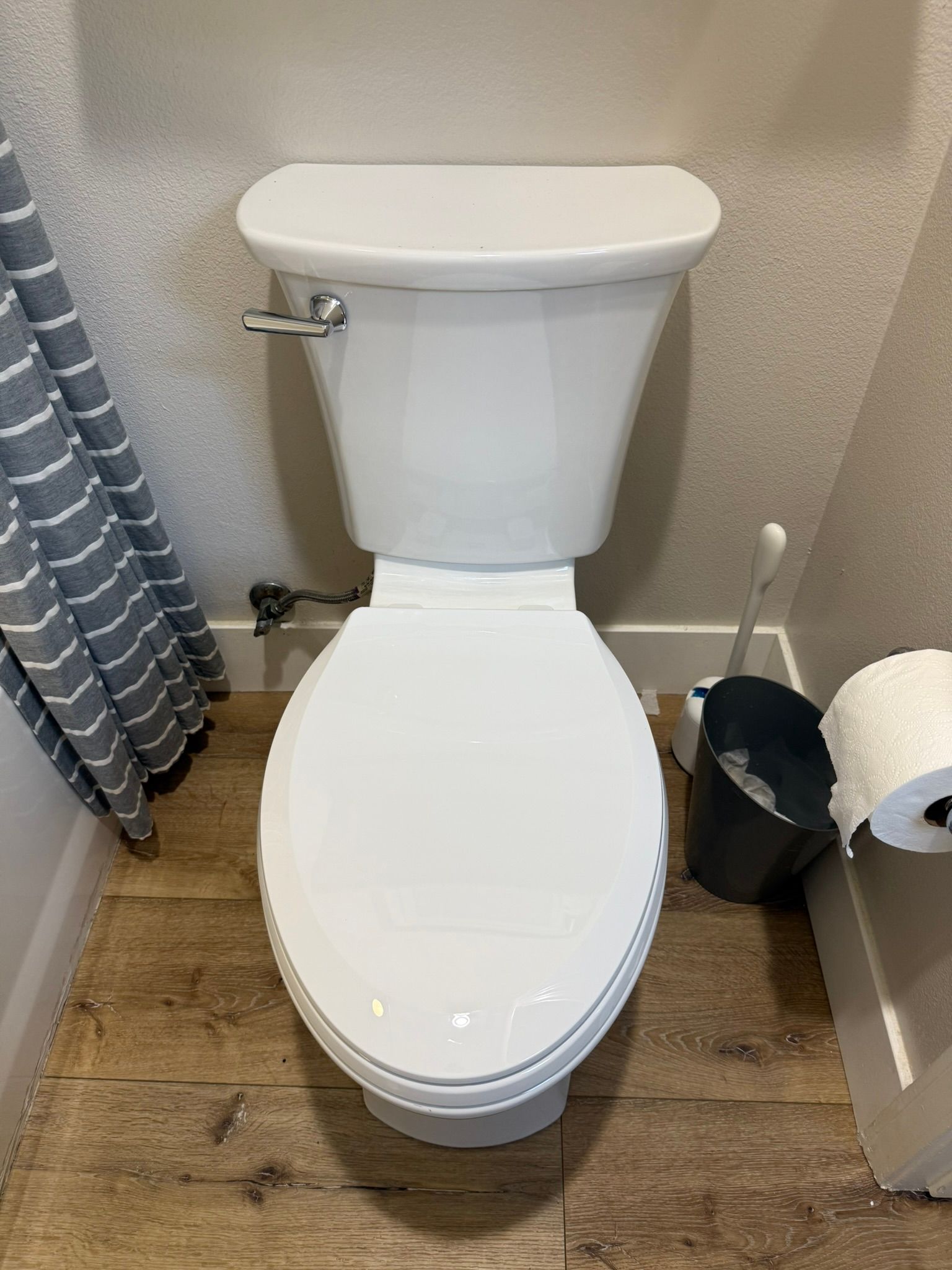 White toilet with closed lid, set against a textured wall, with a toilet brush and roll of toilet paper nearby.