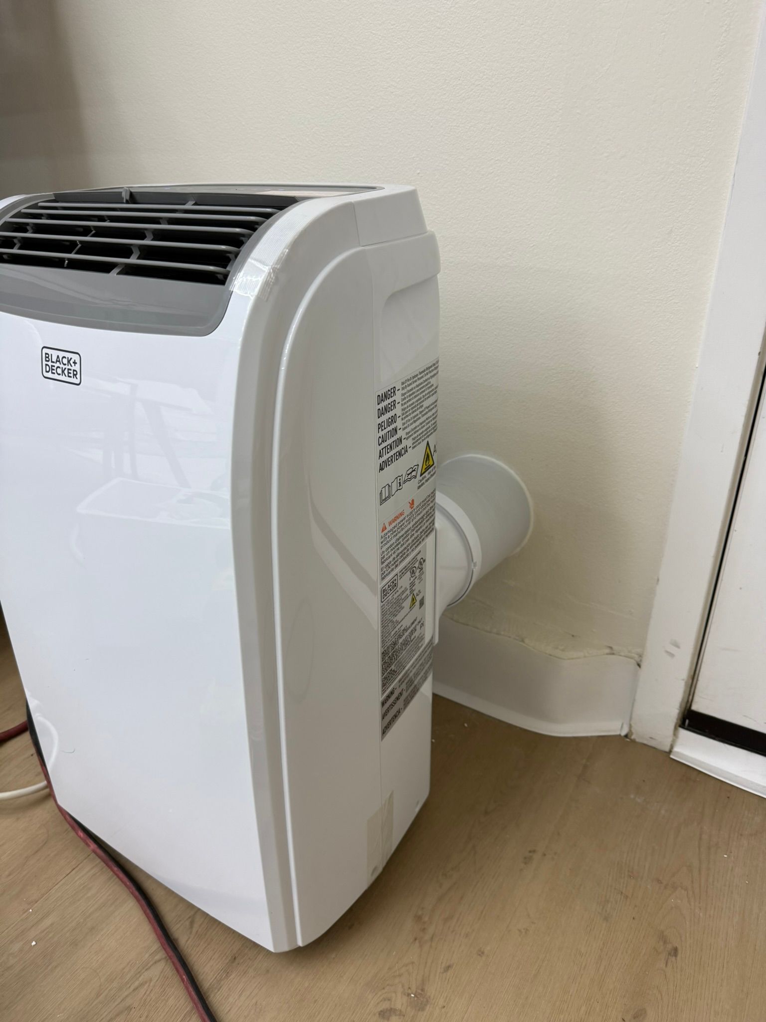 White portable air conditioner with exhaust hose against a wall.