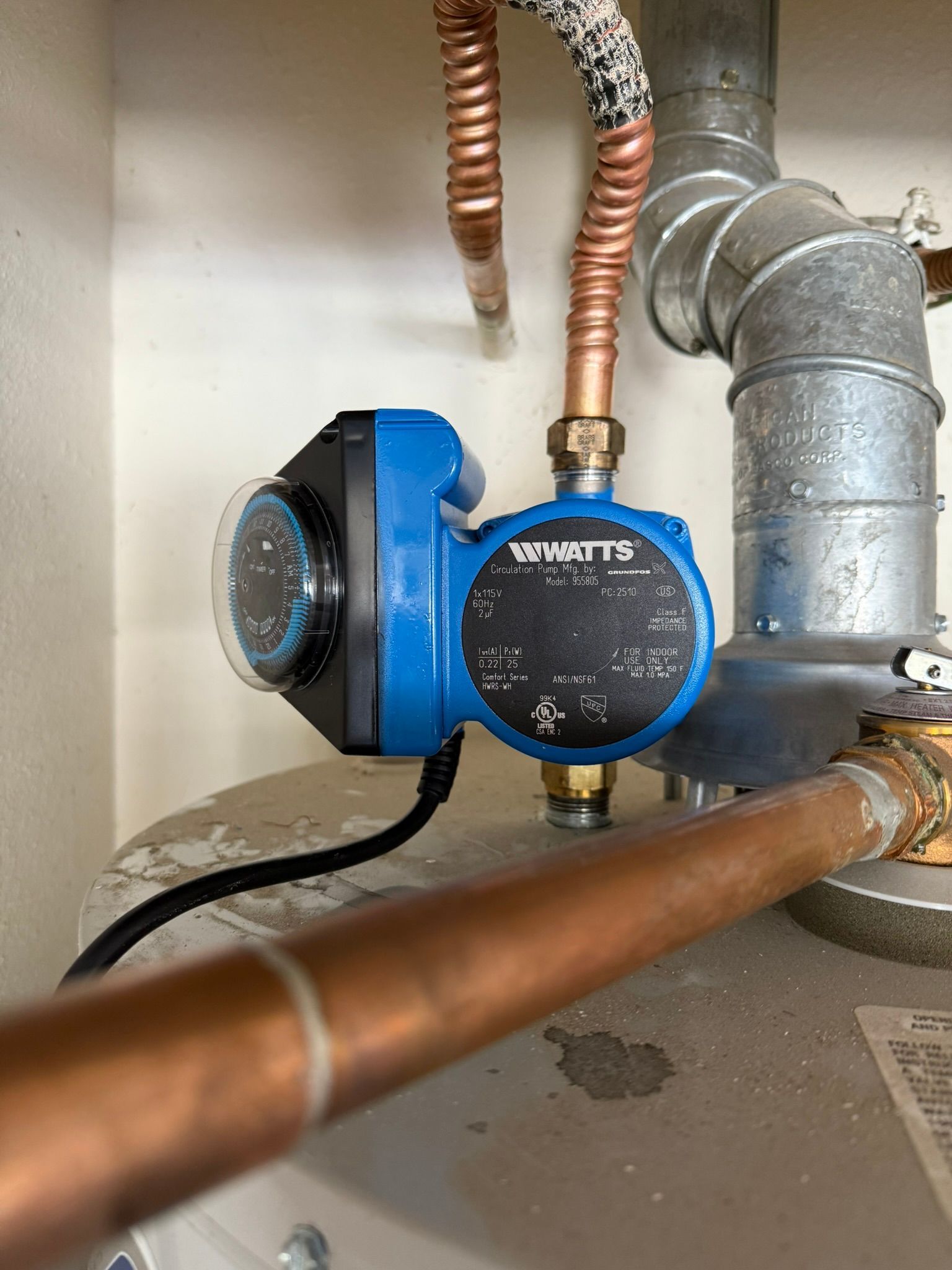 Blue and black Watts brand water heater circulator pump on a water heater, copper and metal pipes.